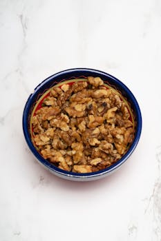 Top view of walnuts in a colorful ceramic bowl on a white marble surface, ideal for food blogs.