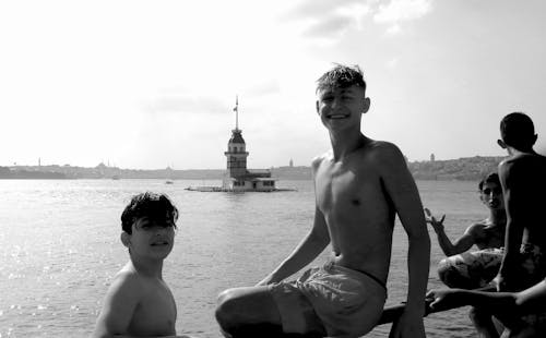 Grayscale Photography of Boys Swimming Near a Lighthouse