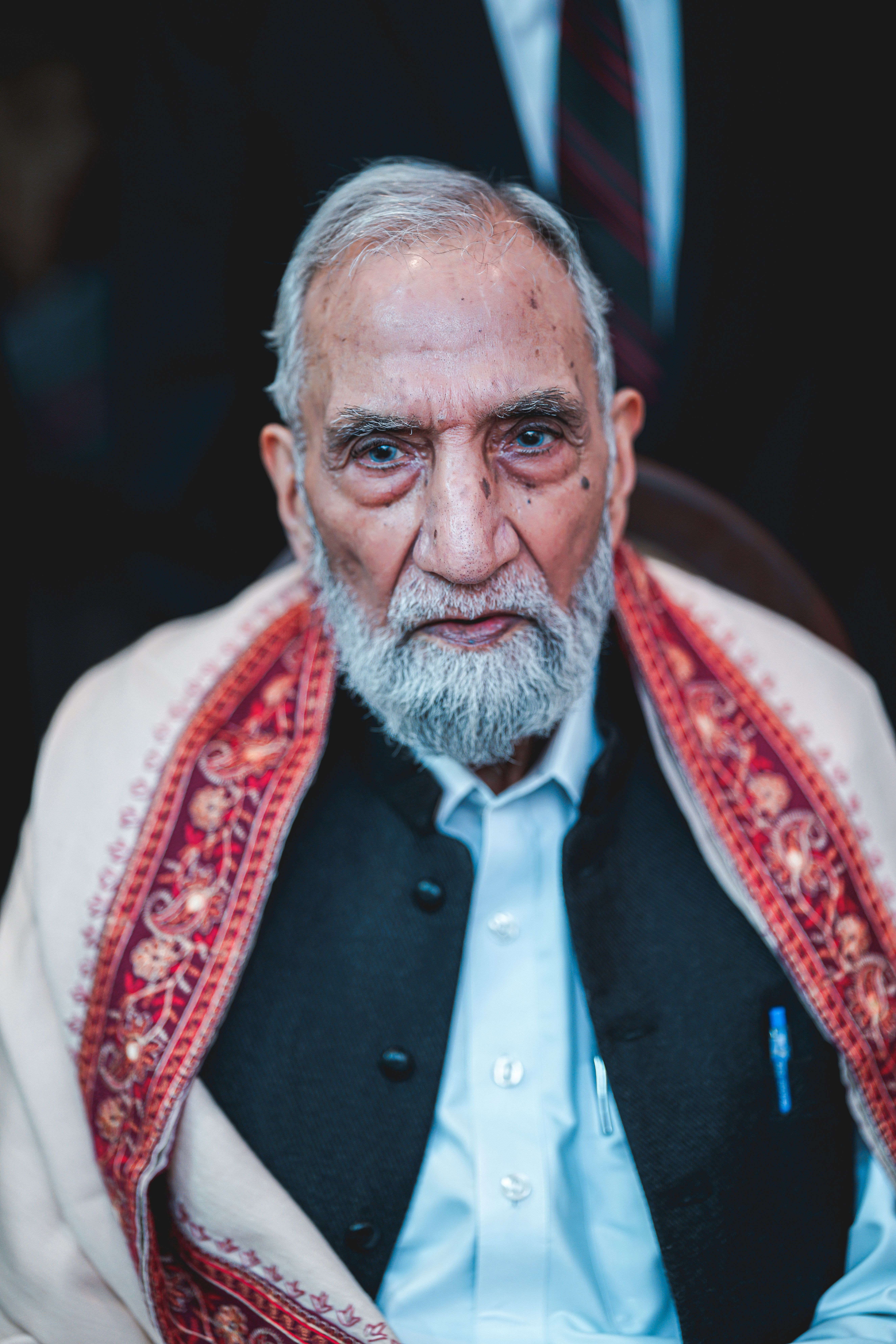 Elderly man with a beard wearing traditional clothing, looking serious.