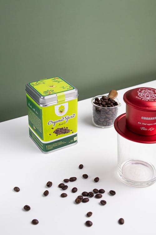 Labeled Can Near Coffee Beans and Glass on a White Surface