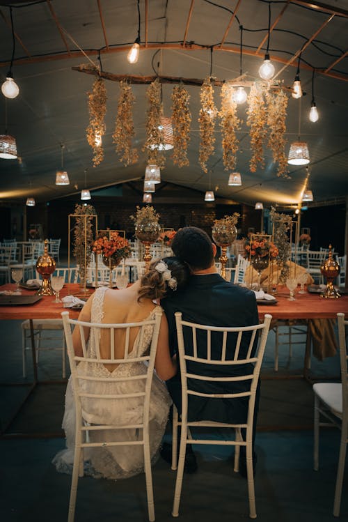 A Newlywed Couple Sitting on a Chair in Front of a Long Table with Elegant Table Setting 