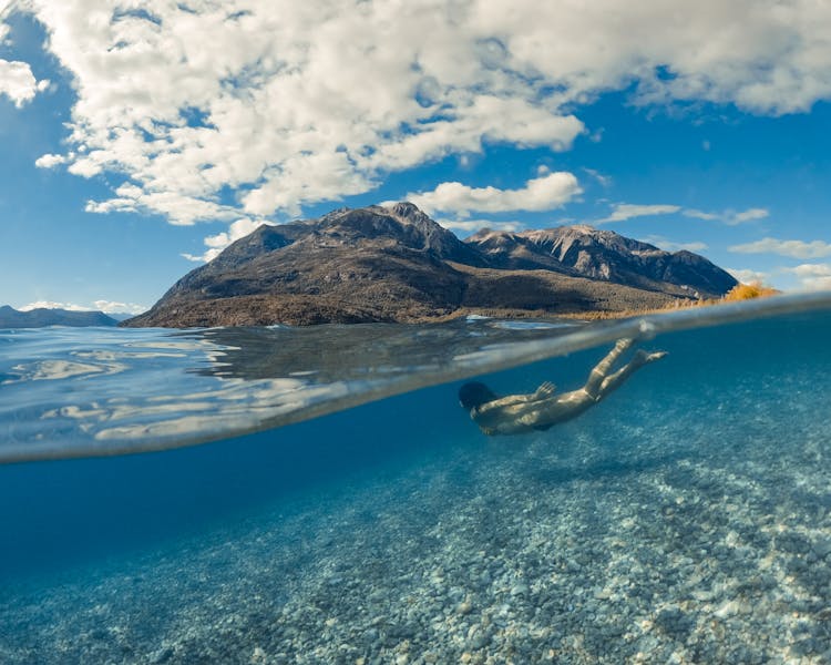 Woman Swimming Underwater In Lake In Mountain Landscape