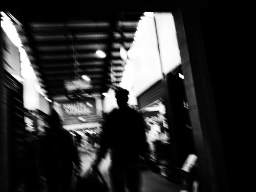 Free Blurry black-and-white image capturing silhouettes walking through an urban corridor, evoking mystery. Stock Photo