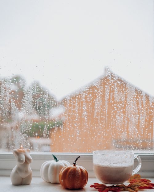 Free A serene autumn moment on a rainy day with coffee, pumpkins, and a candle on a windowsill. Stock Photo