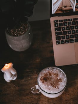 A warm, inviting workspace featuring a cup of coffee, laptop, and candle on a wooden table.