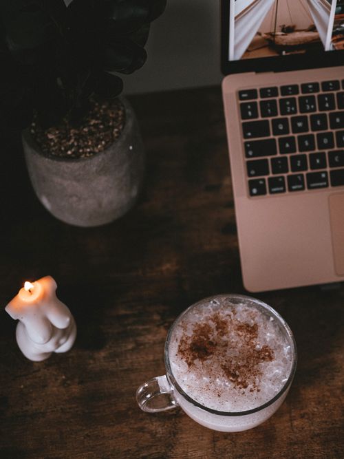 Free A warm, inviting workspace featuring a cup of coffee, laptop, and candle on a wooden table. Stock Photo