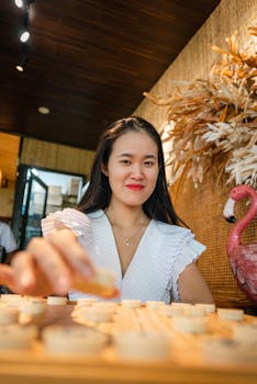 A smiling Asian woman with black hair plays a board game indoors, exuding joy and relaxation.