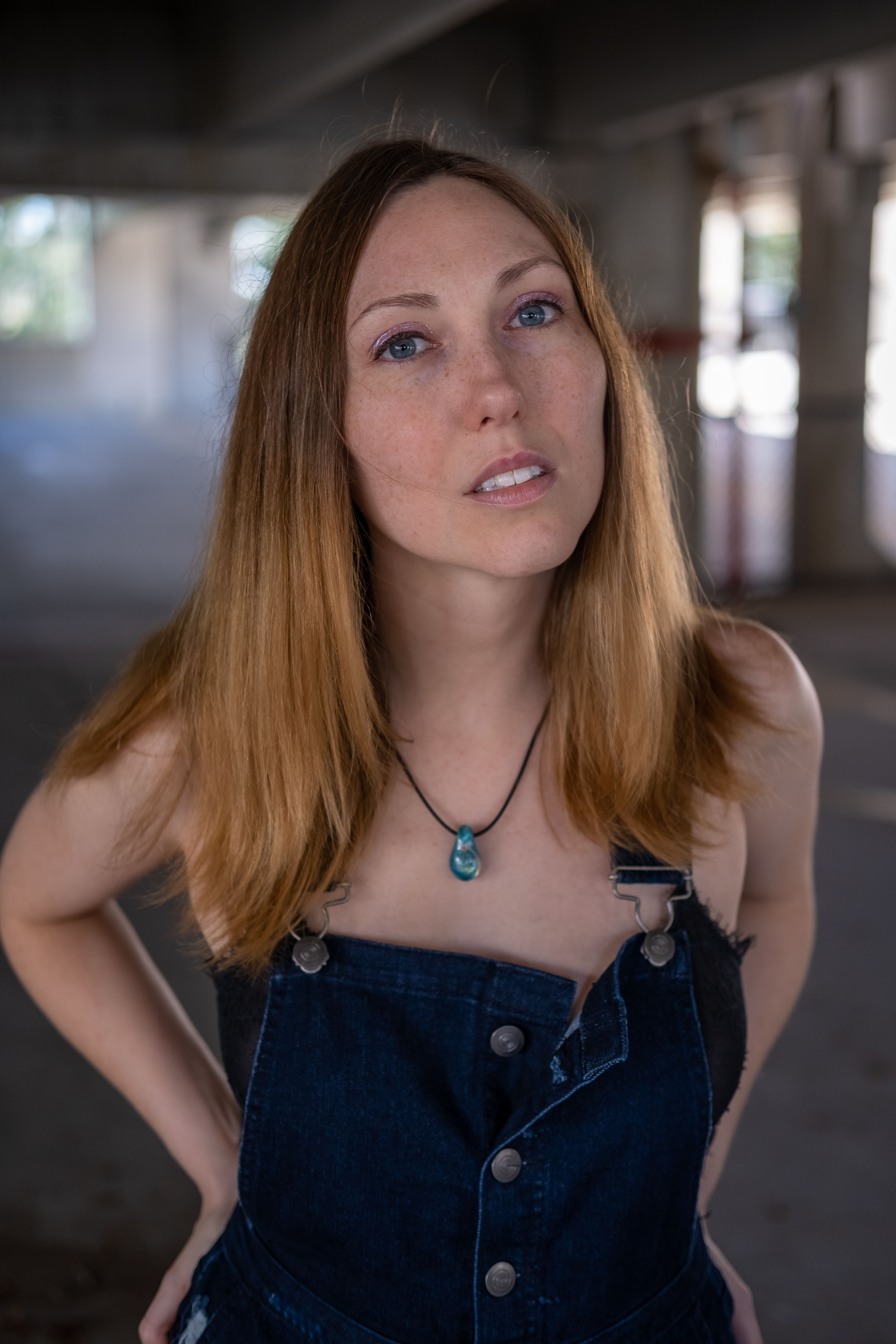 Casual portrait of a woman in a denim outfit under an urban overpass, exuding confidence and style.