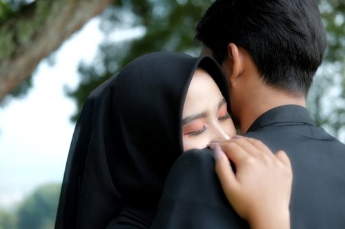 Free A close-up of an Asian couple embracing tenderly under a tree, conveying warmth and love. Stock Photo