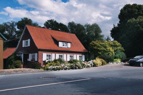 Free A picturesque brick house with a red roof surrounded by vibrant greenery on a sunny day. Stock Photo