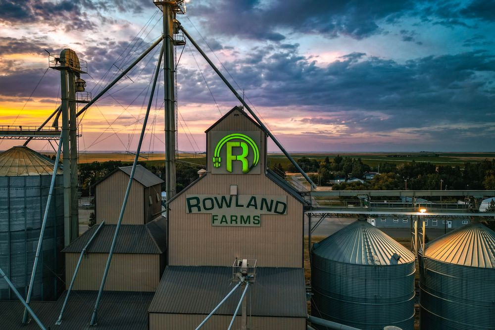 Aerial view of Rowland Farms with silos and industrial structures against a vibrant sunset in Taber, Alberta, Canada.
