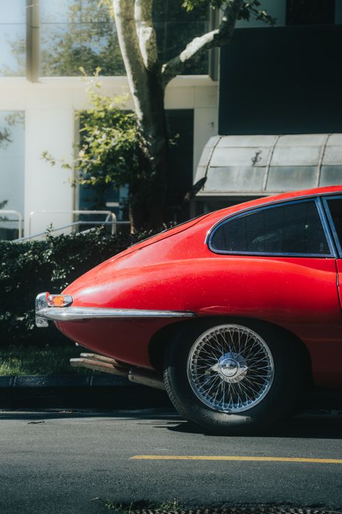 Free Rear view of a vibrant red vintage car parked on an asphalt road during the day. Stock Photo