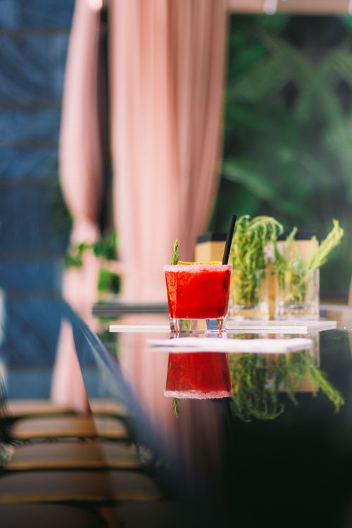 Free Close-up of a vibrant red cocktail with herbs on a sleek bar table, reflecting an upscale ambiance. Stock Photo