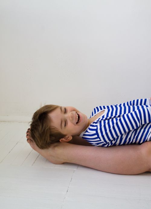Free Joyful child wearing a striped shirt, playfully lying indoors with a bright white background. Stock Photo