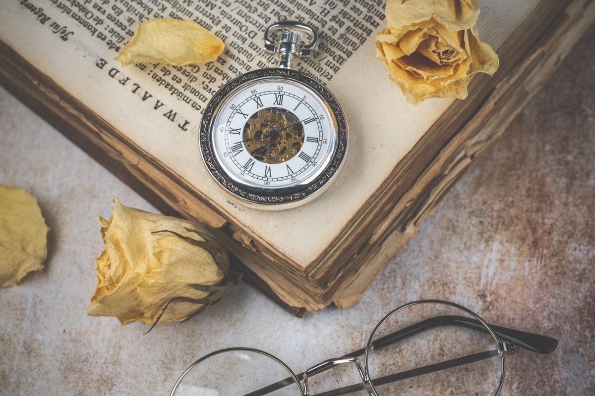 A vintage pocket watch resting on an open antique book beside dried yellow roses