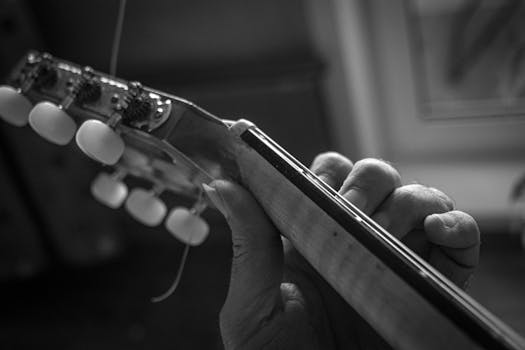 Monochrome image capturing a hand playing a guitar close-up.