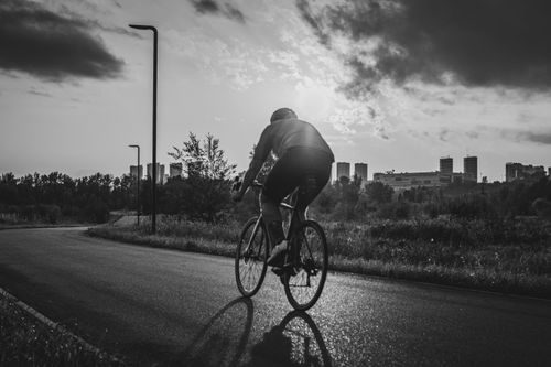 Free A cyclist rides on a road with an urban skyline backdrop in black and white. Stock Photo