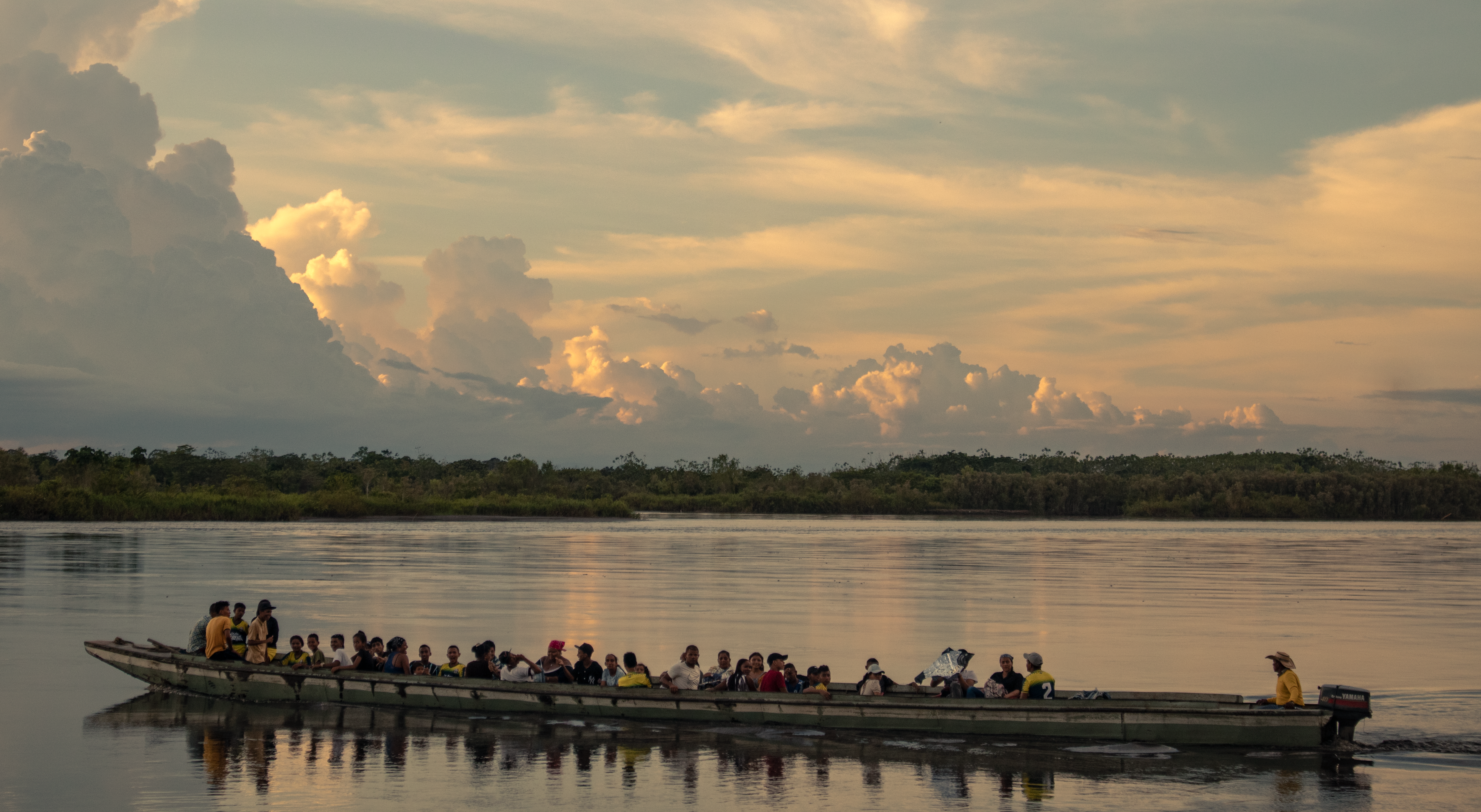 Serene image of a boat carrying people at sunset on a tranquil Colombian river.