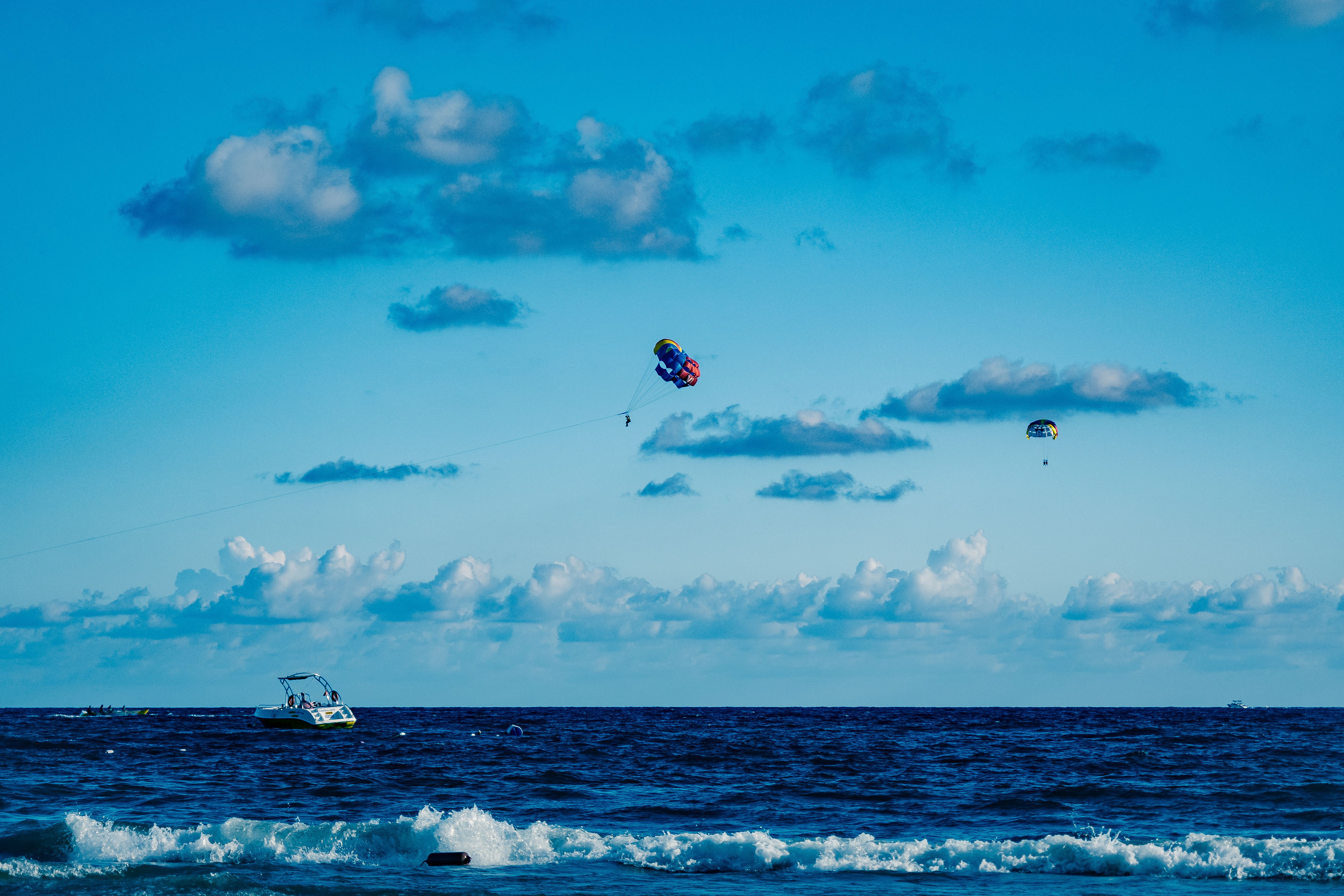 Experience the thrill of parasailing over the ocean with boats and crashing waves beneath a clear su