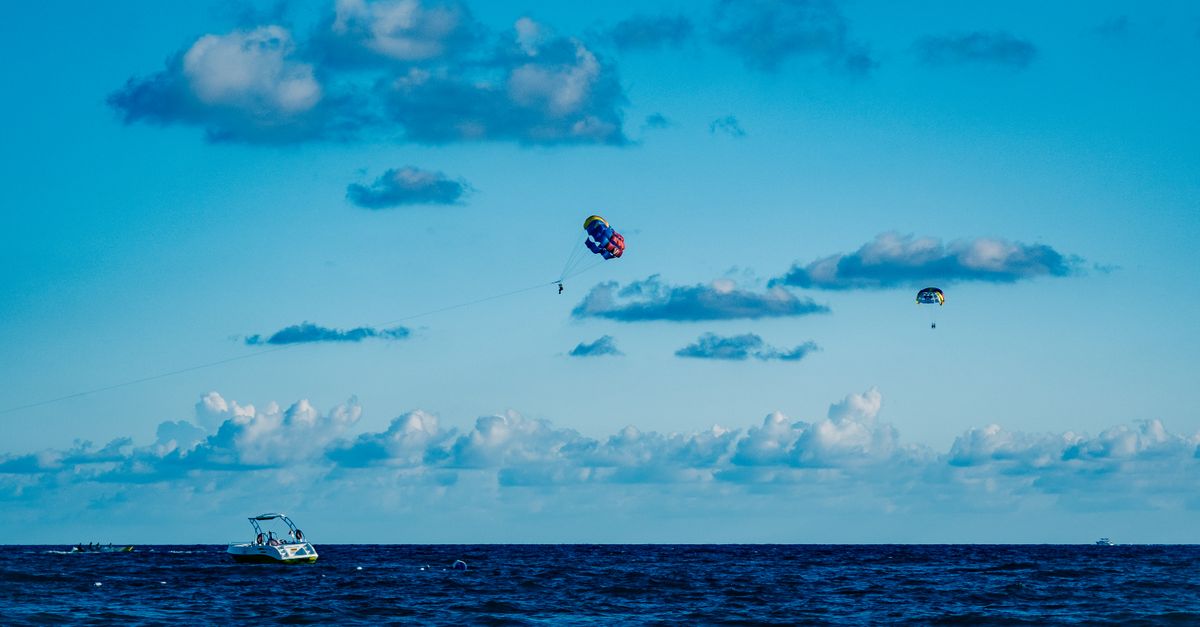 Experience the thrill of parasailing over the ocean with boats and crashing waves beneath a clear su