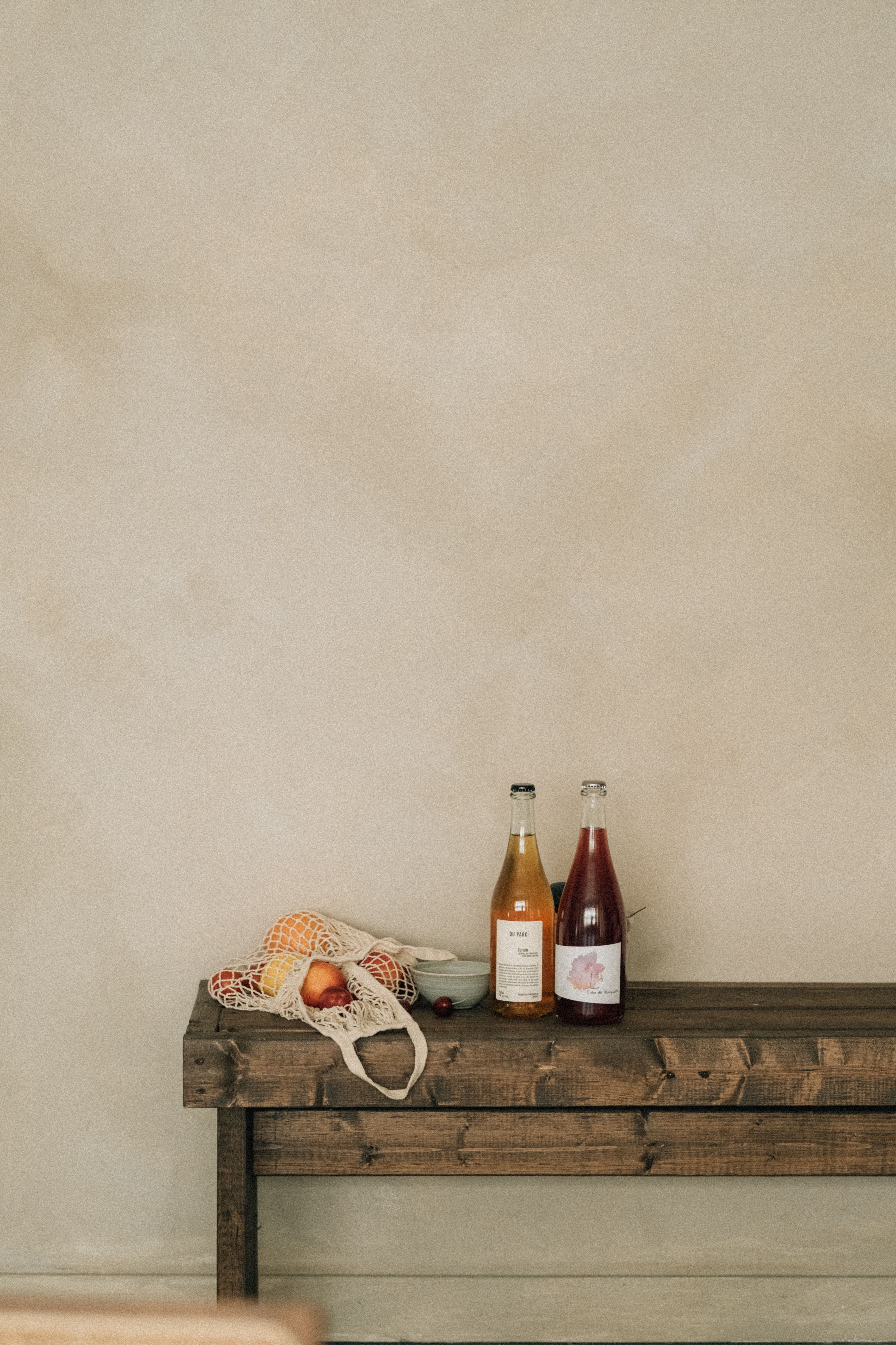 A minimalist bench setup featuring two bottles and a mesh bag of fruits, ideal for still life themes.