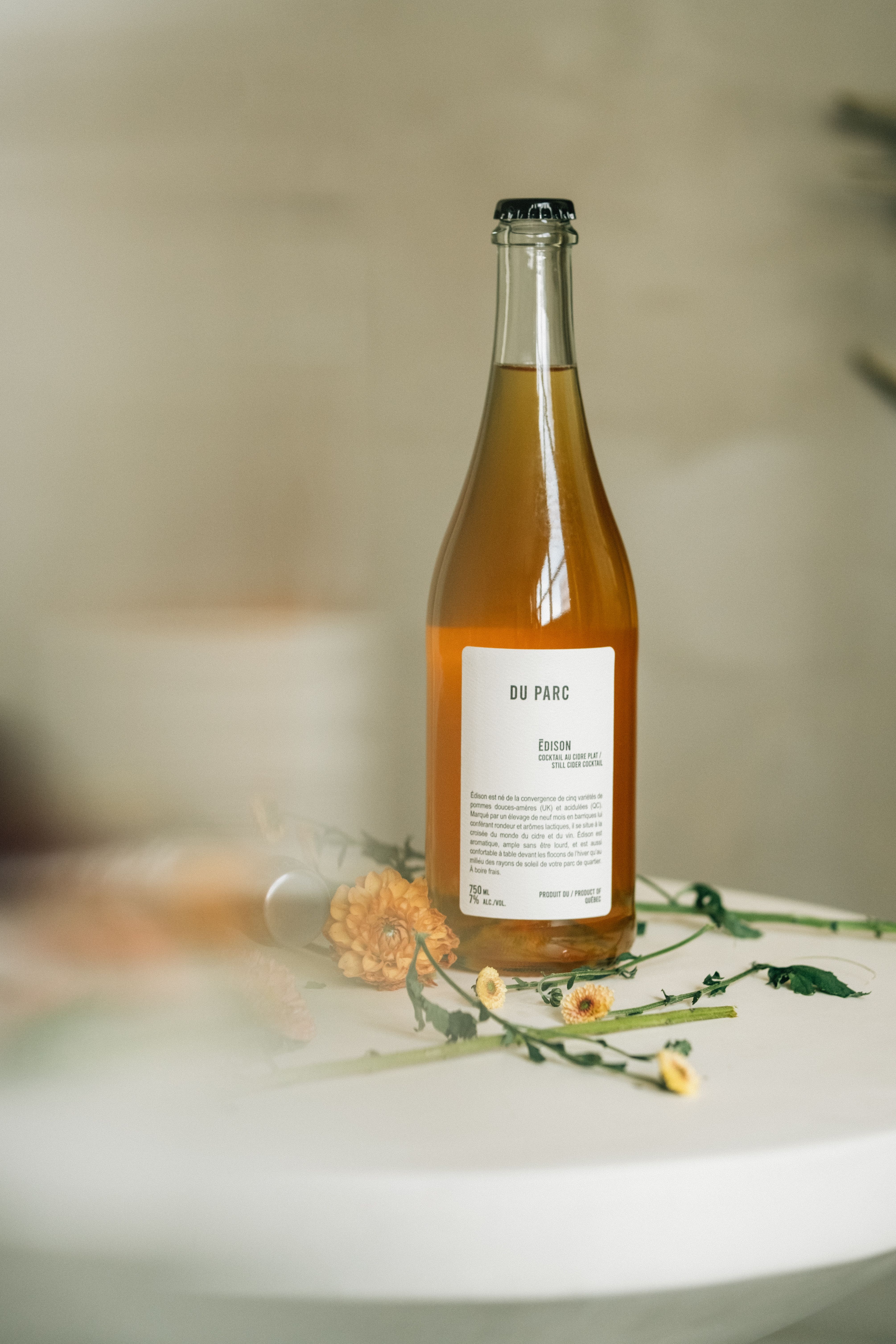 A stylish beverage bottle on a white table decorated with soft-focus flowers.