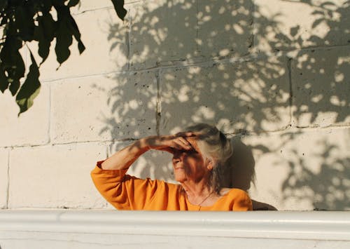Elderly Woman in Orange Shirt Leaning on the Wall