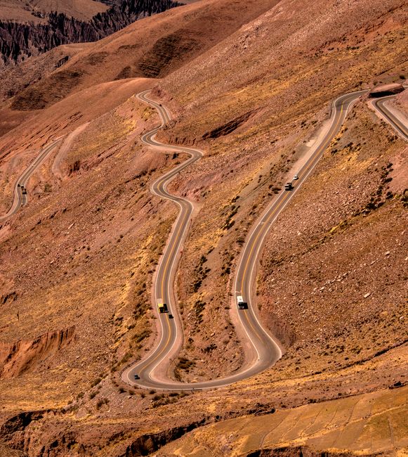 Aerial view of a winding road with cars navigating through a mountainous desert landscape.