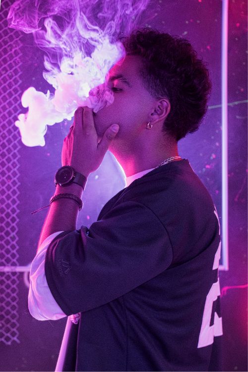 Free A young man in casual urban attire vaping against a neon-lit setting in Bogotá, Colombia. Stock Photo