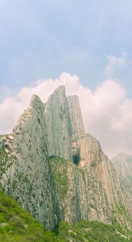 Stunning vertical shot of towering rock formations against blue sky and white clouds.