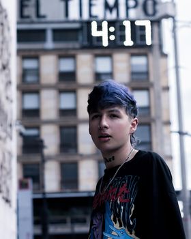 Young adult with piercings in Bogotá's urban setting, building clock visible.