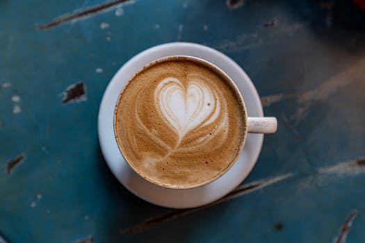 Top view of a latte with heart-shaped foam art on a blue ceramic table.
