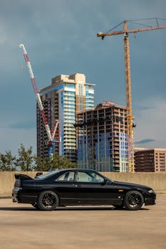 Side view of a black Nissan Skyline GTR parked with skyscrapers under construction in Austin, TX.