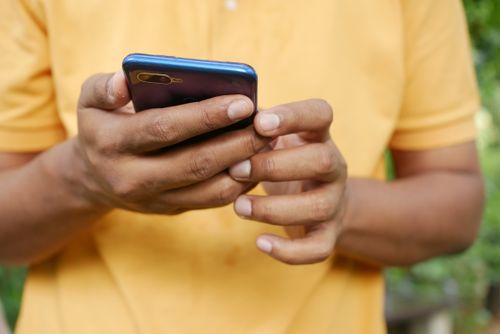 Free Close-up of a person in an orange shirt using a smartphone outdoors. Stock Photo