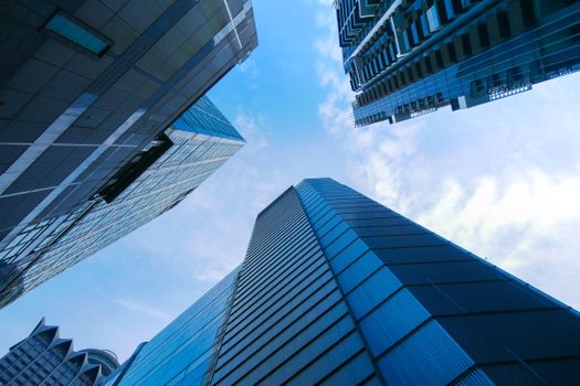 Low angle view of modern skyscrapers against a bright blue sky with clouds, showcasing contemporary architecture.
