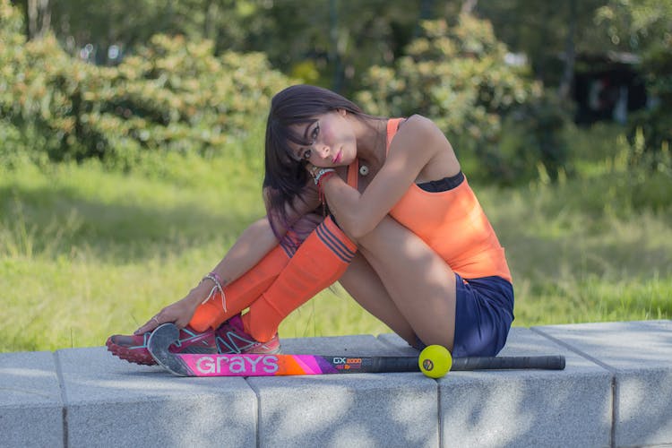 A Woman In Orange Tank Top Sitting On Concrete Bench