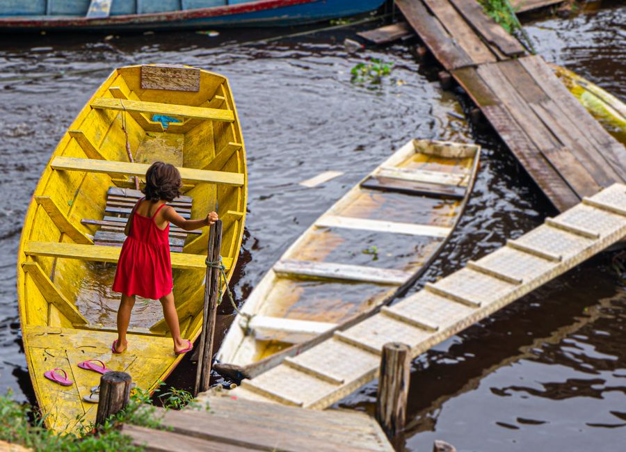 Young girl in red dress navigating a yellow boat on a river in Manaus, Brazil.