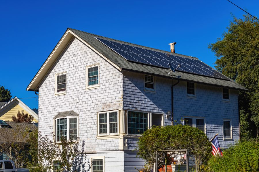 A modern two-story home with solar panels on its roof under a clear blue sky.