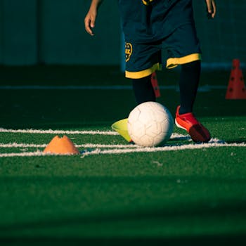 Young player practicing soccer skills on a field with cones during daytime.