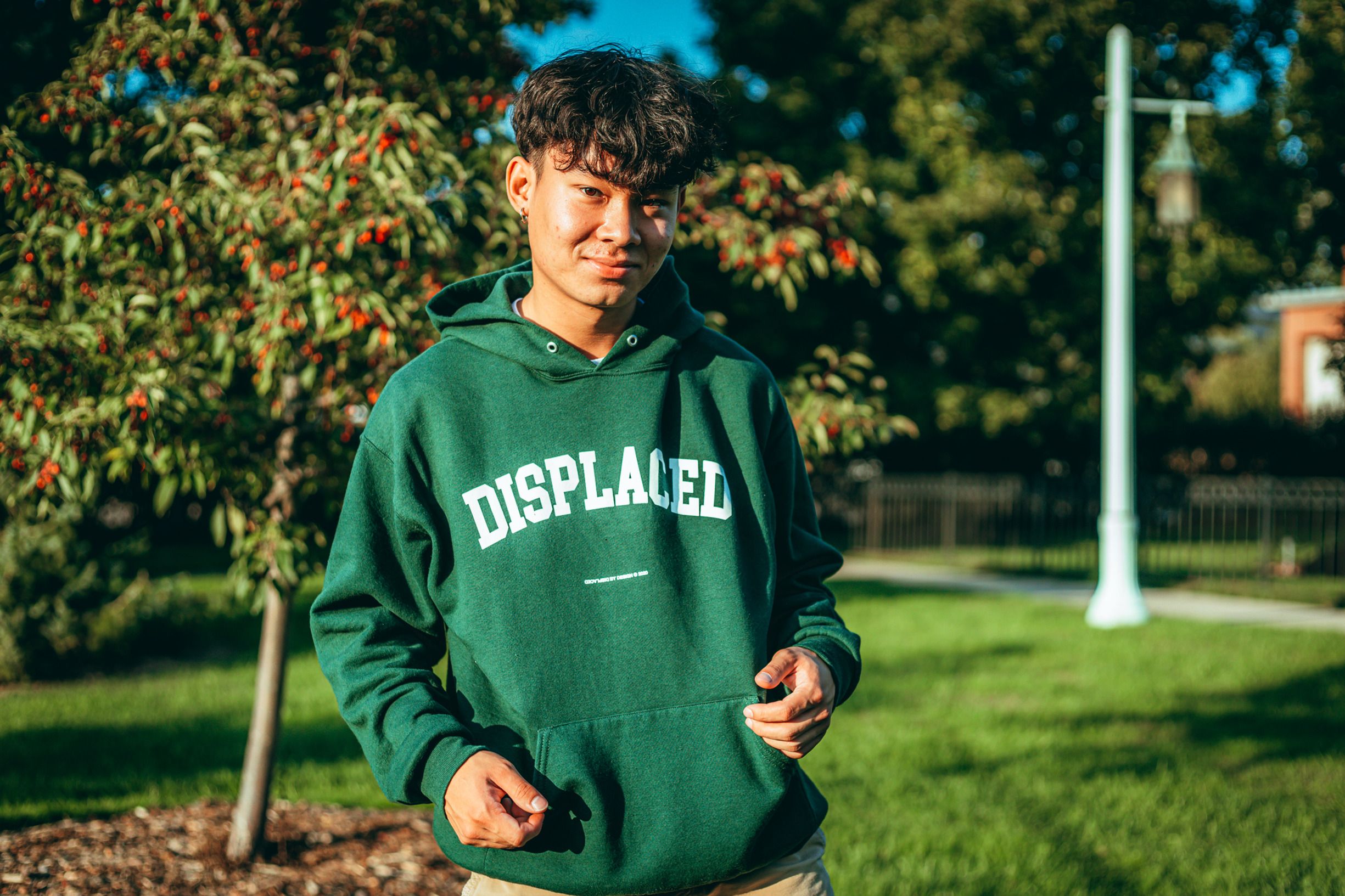 Young man in green hoodie smiling in a sunny park setting.