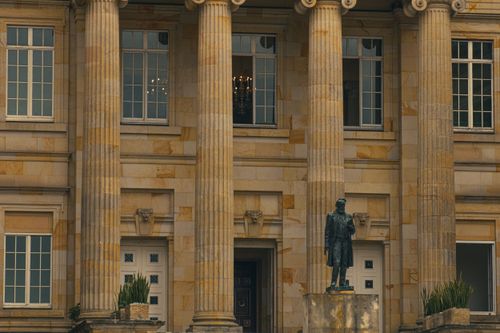 Free Elegant view of a classical building with pillars and a statue at the entrance. Stock Photo
