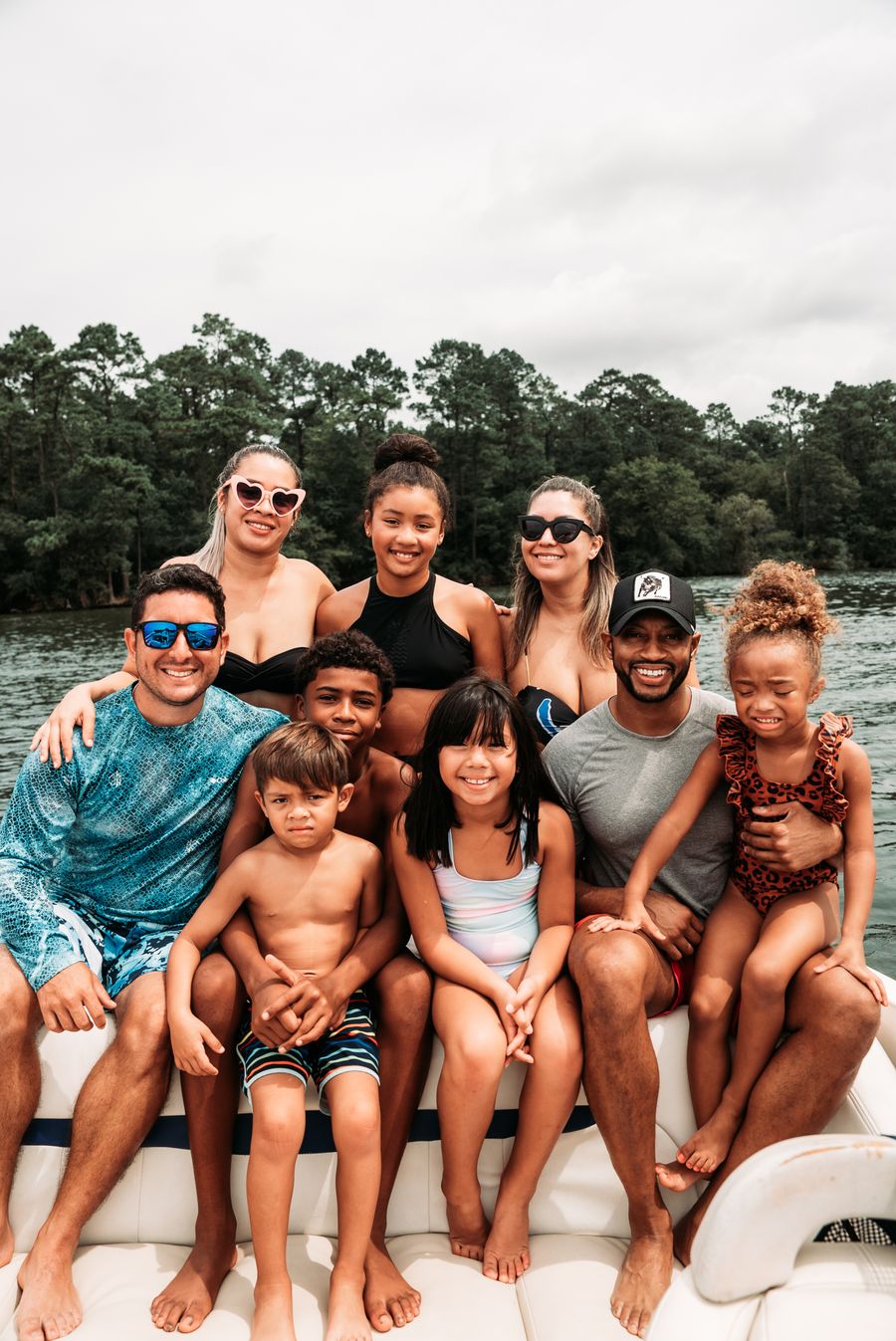 A big, smiling group of family and friends on a boat on a tree-lined lake
