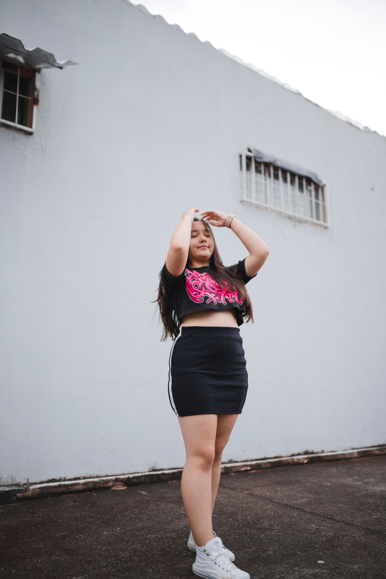 Woman in a black cropped graphic tee and black mini skirt with white sneakers