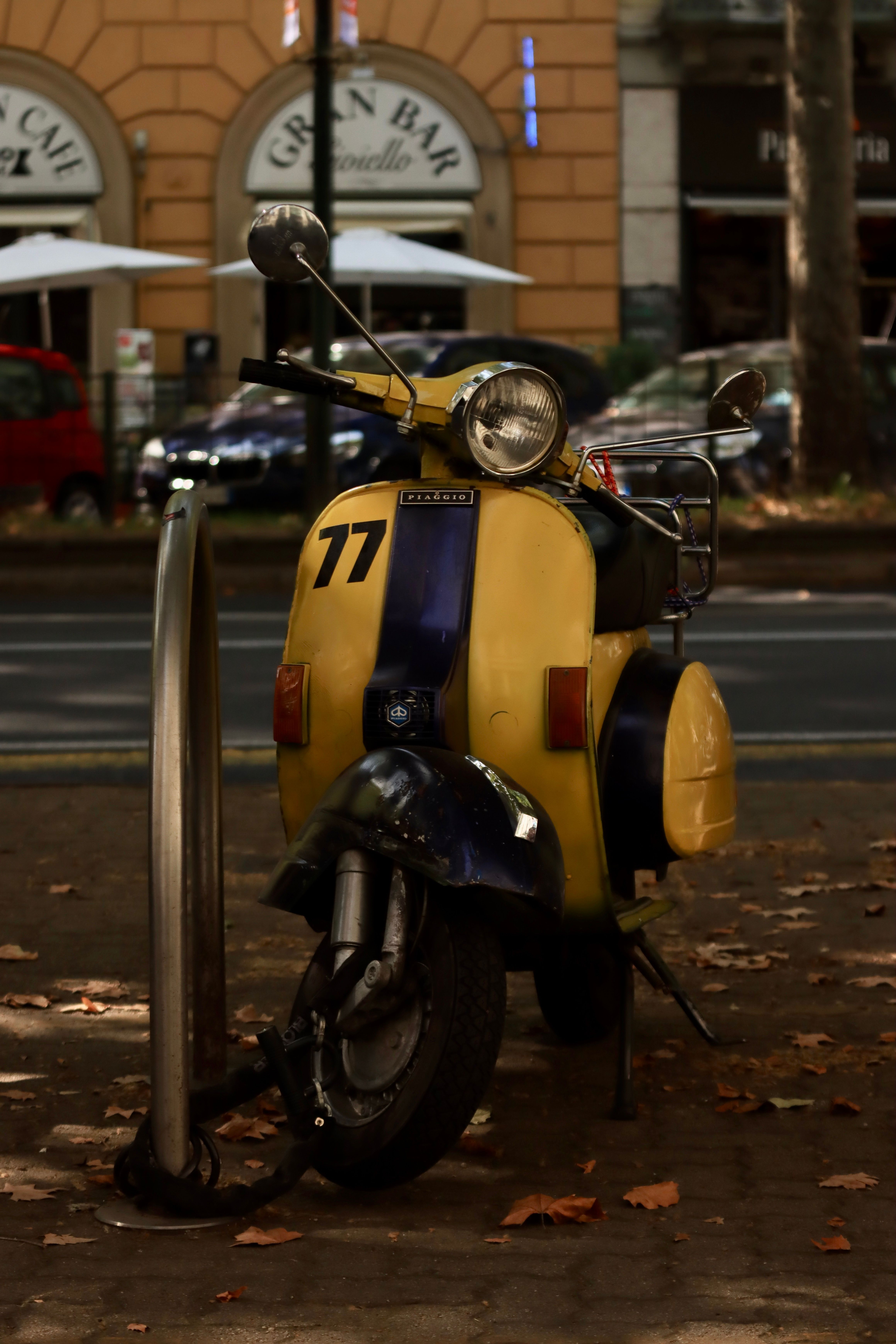 Yellow and blue vintage scooter parked on a street in Turin, Italy, next to a city cafe.