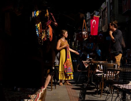 A colorful street market scene in Istanbul with people shopping and Turkish flags displayed.