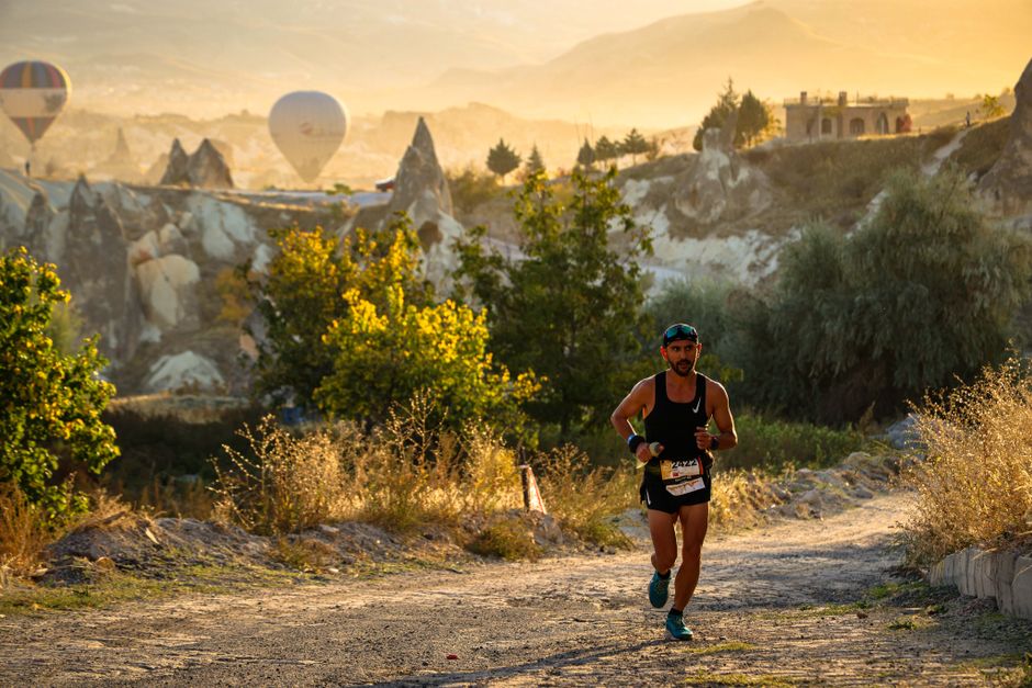 A marathon runner on a scenic trail in Cappadocia with hot air balloons in the background.