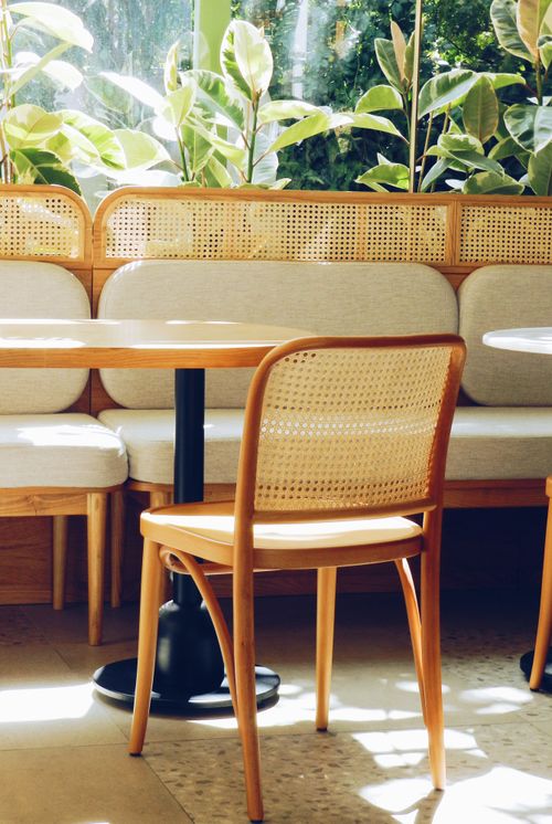 Free Cozy café interior featuring a sunlit wicker chair and wooden table setup. Stock Photo