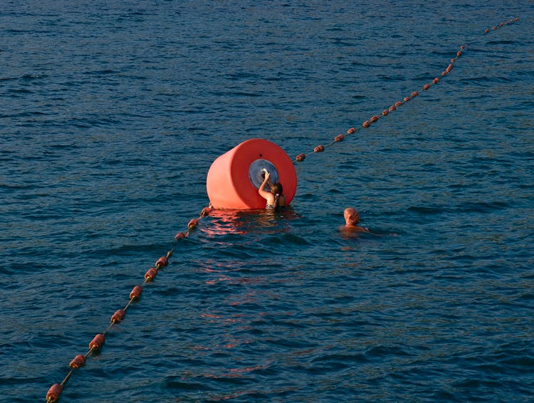 People Swimming At Sea Near Buoy