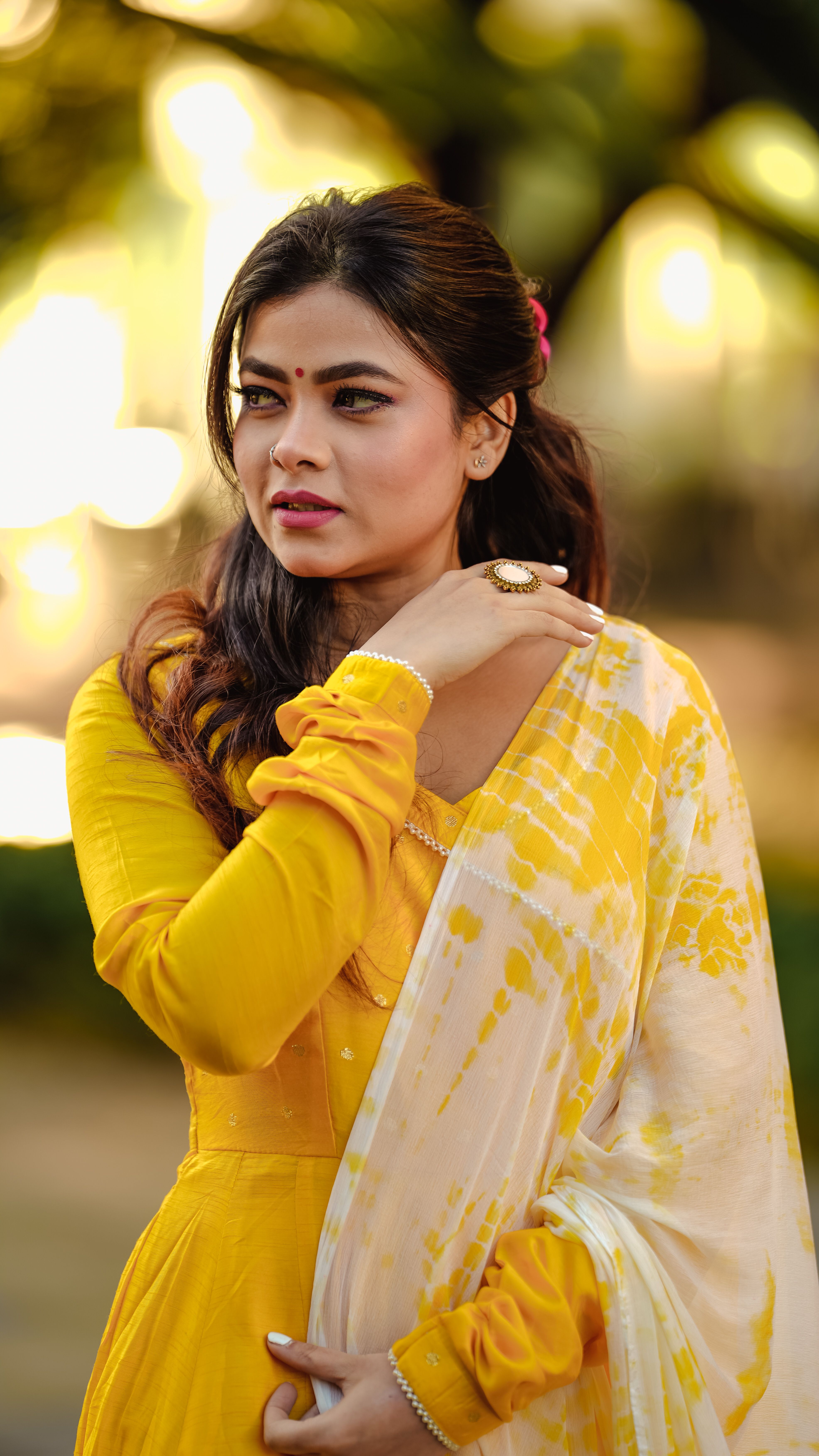 Portrait of a South Asian woman in yellow traditional attire outdoors with a blurred background.
