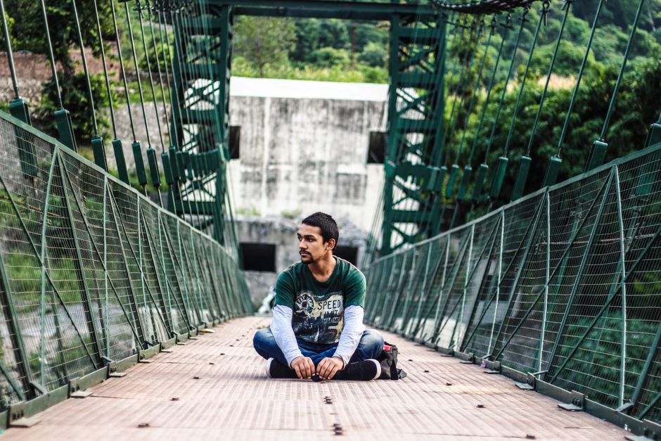 A man sits meditatively on a suspension bridge surrounded by nature.
